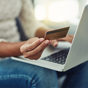 Woman with a laptop on her lap holding up a credit card. Her face is not visible.